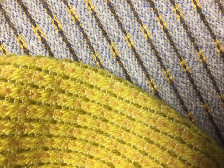 Tekstilmønster med diagonale striper i blått og gult. Ullstoff i nærbilde, gule og beige nyanser av garn.