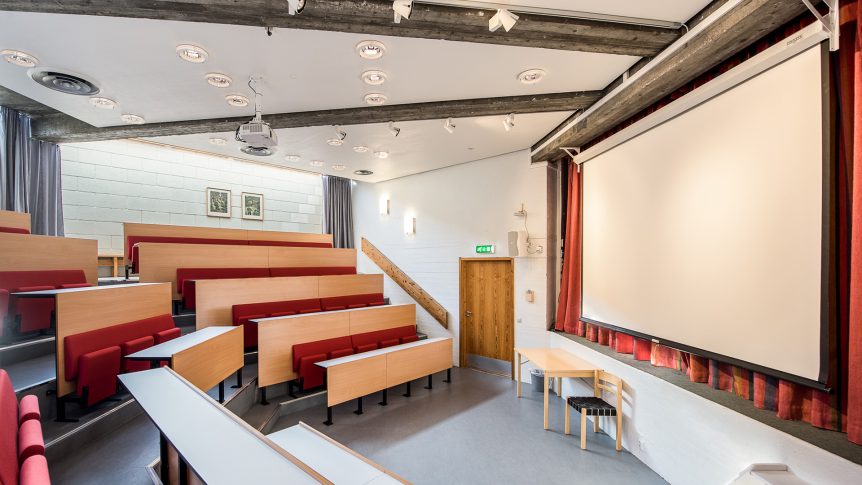 Et lyst auditorium med trebenker og projektorskjerm, klare for forelesninger.