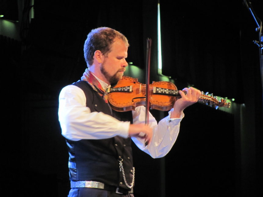 En musiker spiller hardingfele på scenen i tradisjonell norsk drakt under en konsert.