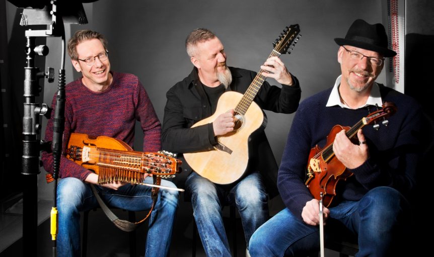 Tre menn spiller tradisjonelle instrumenter: gitar, nyckelharpa og fele, i studioopptak med fokus på musikkglede.