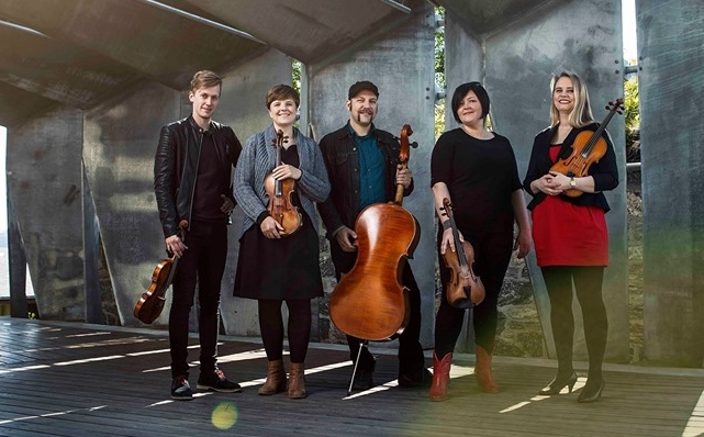 Gruppe på fem musikere med strykere i en moderne arkitektonisk setting, instrumenter inkluderer fioliner og cello.