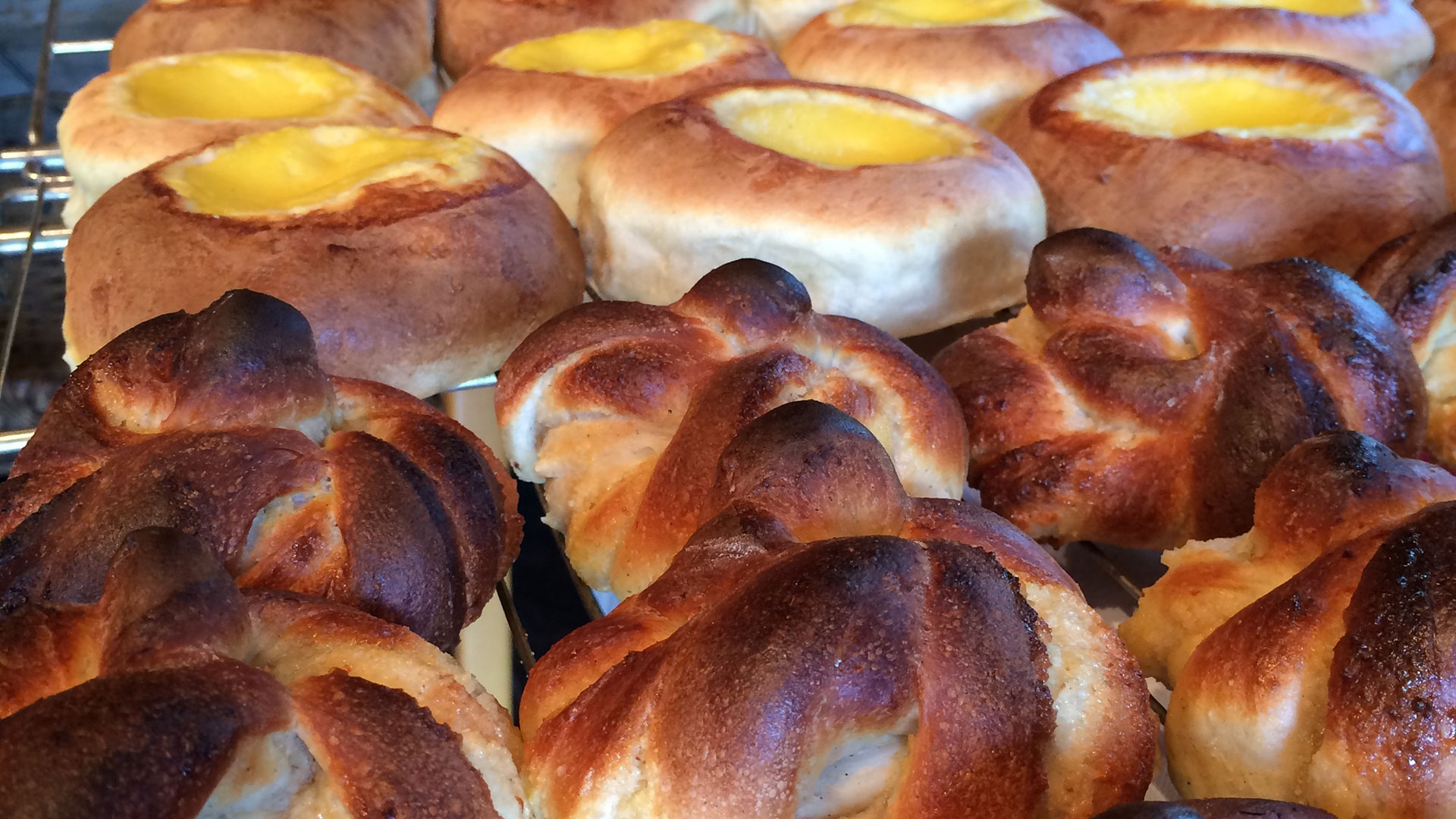 Friske, gyldenbrune boller og skoleboller med vaniljekrem på en bakerist.