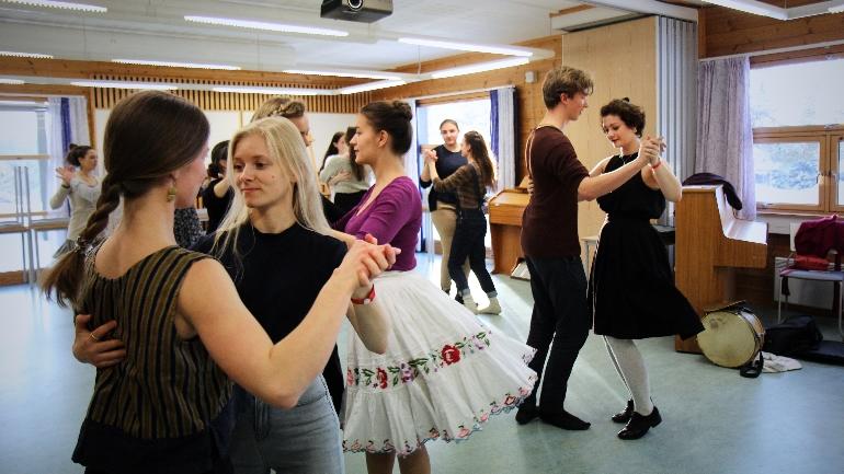 Unge mennesker danser i en lys dansesal, kledd i uformelle og fargerike klær.