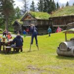Familieaktiviteter ved gamle tømmerhus og lekeplass med stilteløping i norsk natur.