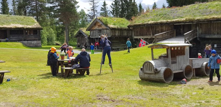 Familieaktiviteter ved gamle tømmerhus og lekeplass med stilteløping i norsk natur.