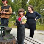 Barn i smedieutstyr med voksen til stede, smiler ved ildstedet i skogen. Klar for smiing og moro.