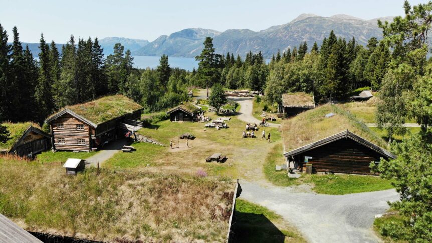 Norsk fjellandskap med tradisjonelle gressdekte hus og utsikt over en innsjø.