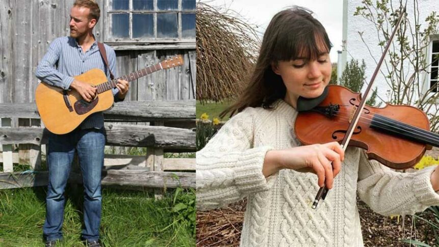 To personer spiller musikk, en mann med gitar og en kvinne med fiolin, utendørs foran en trebygning.