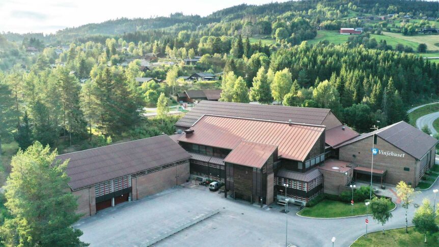 Ikke tilgjengelig som personidentifikasjon: Vinjehuset omgitt av frodig, norsk landskap med skog og åser i bakgrunnen.