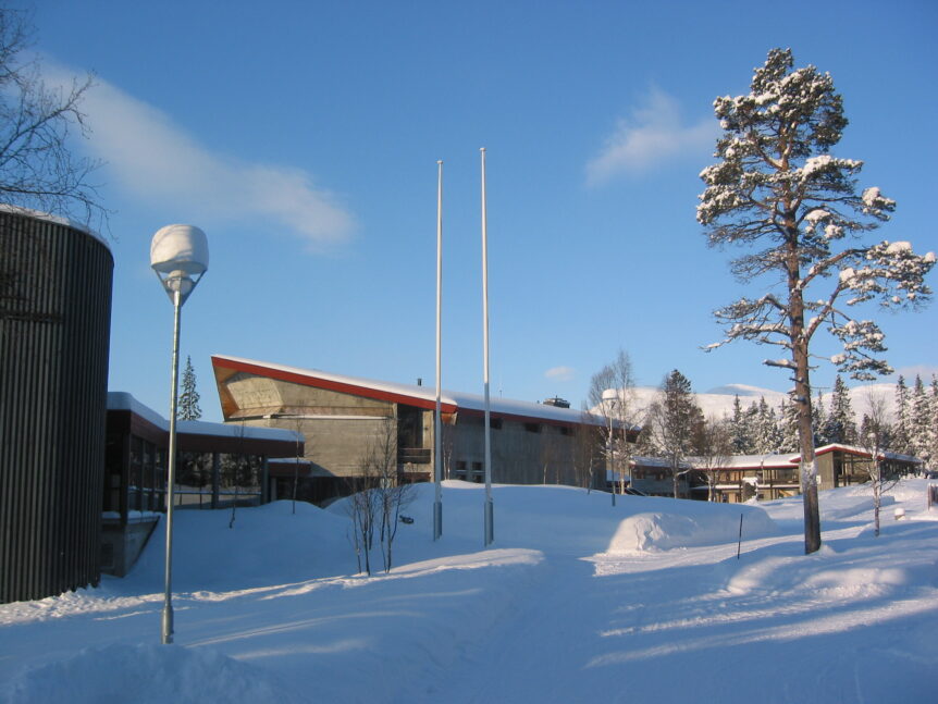 Moderne bygning omgitt av snø og vinterlandskap, klar blå himmel, trær med snø.