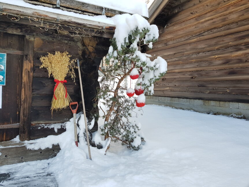 Snødekt hytte med julenek, snøspade og pyntet grantrær. Vinteridyll og tradisjonelle juledekorasjoner i Norge.