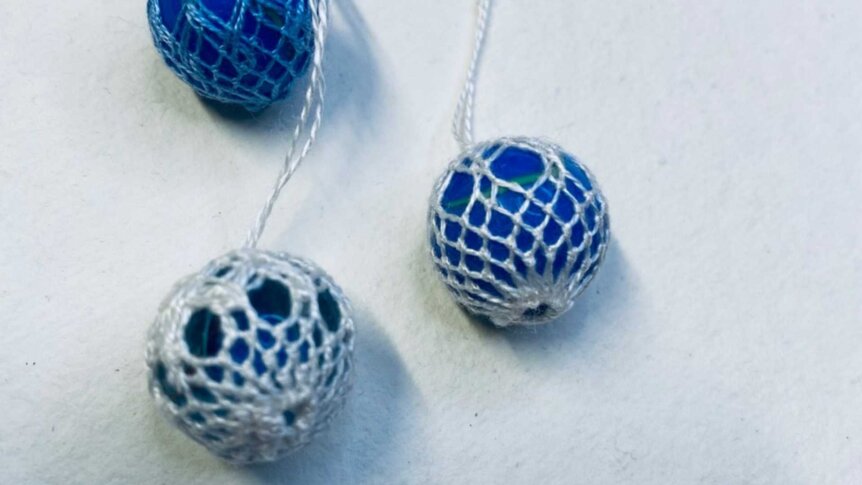 Blå perler i heklet netting, tre stykker, på hvit bakgrunn. Håndlagde dekorasjoner med delikat mønster.