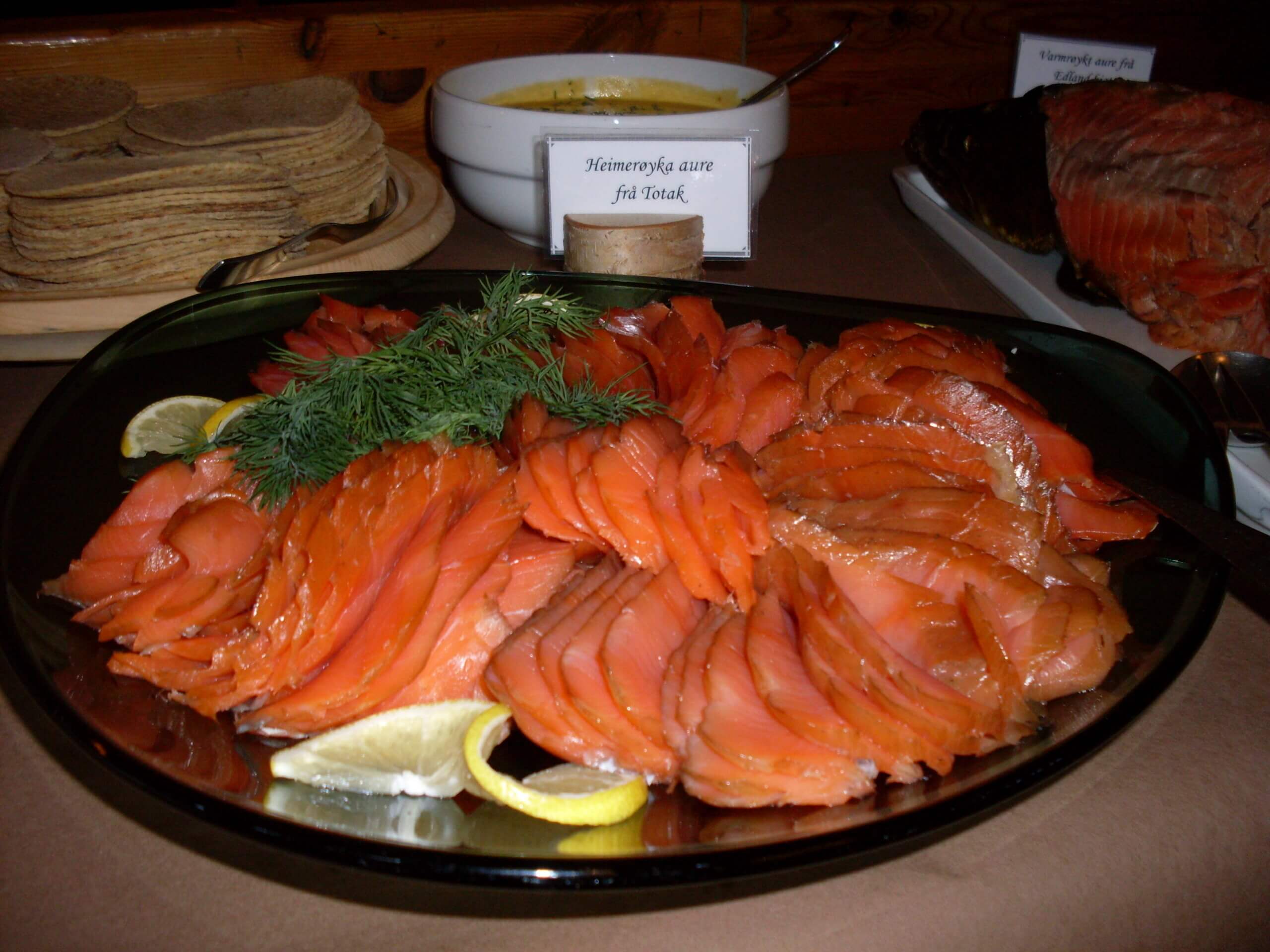 Tallerken med røkt laks, sitron og dill, servert med flatbrød og suppe i bakgrunnen.