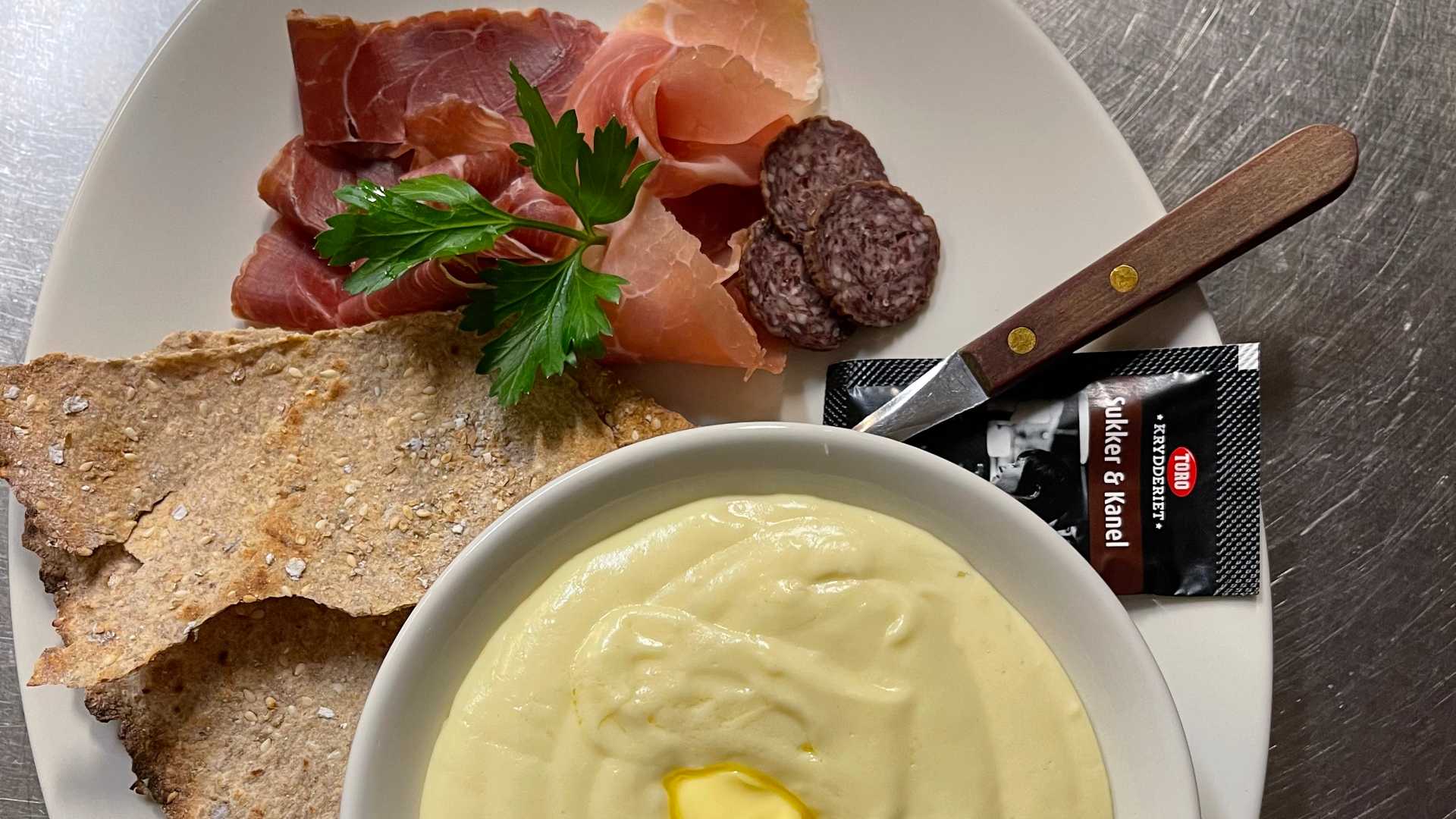 Kjøttfat med spekeskinke, salami, flatbrød og grøt med smør serveres på tallerken, dekorert med persille.