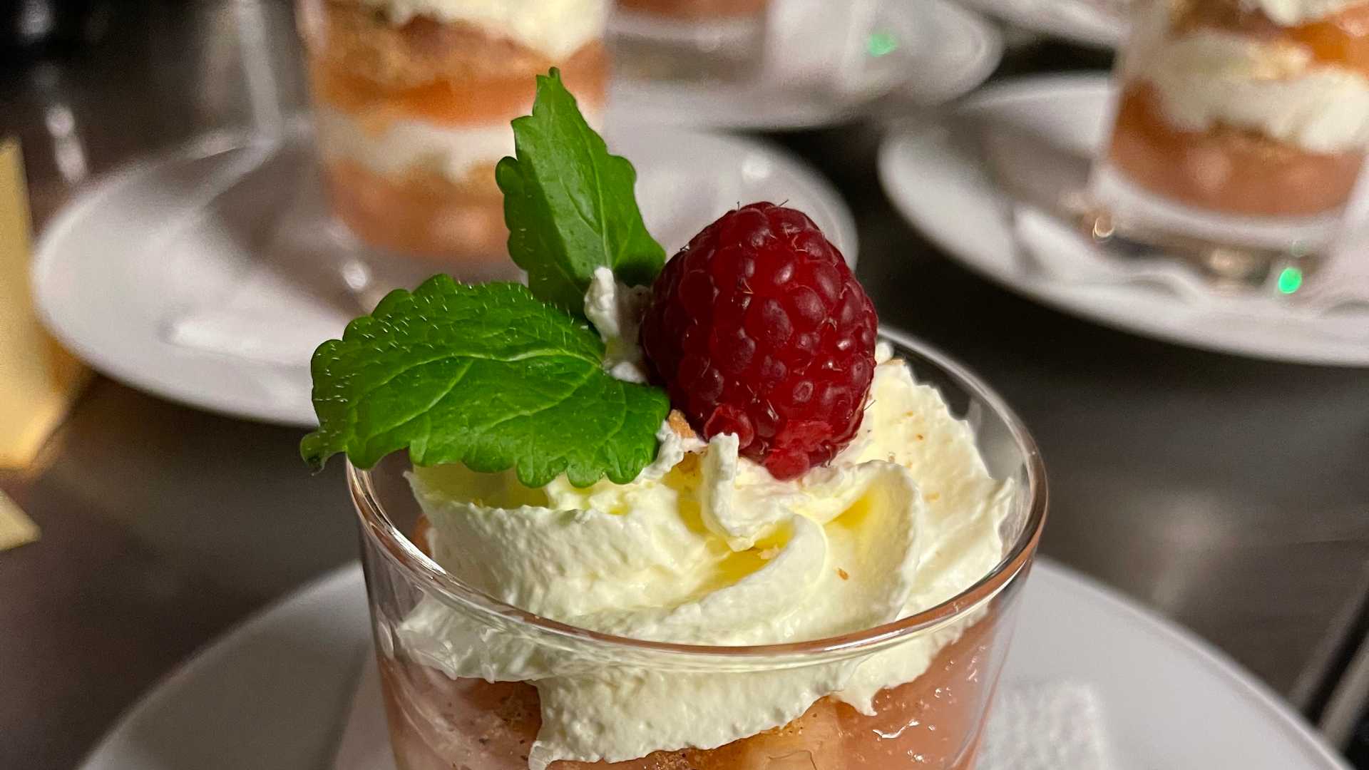 Dessert i glass med bringebær, krem, og mynte, servert på middagstallerken. Perfekt for spesielle anledninger.