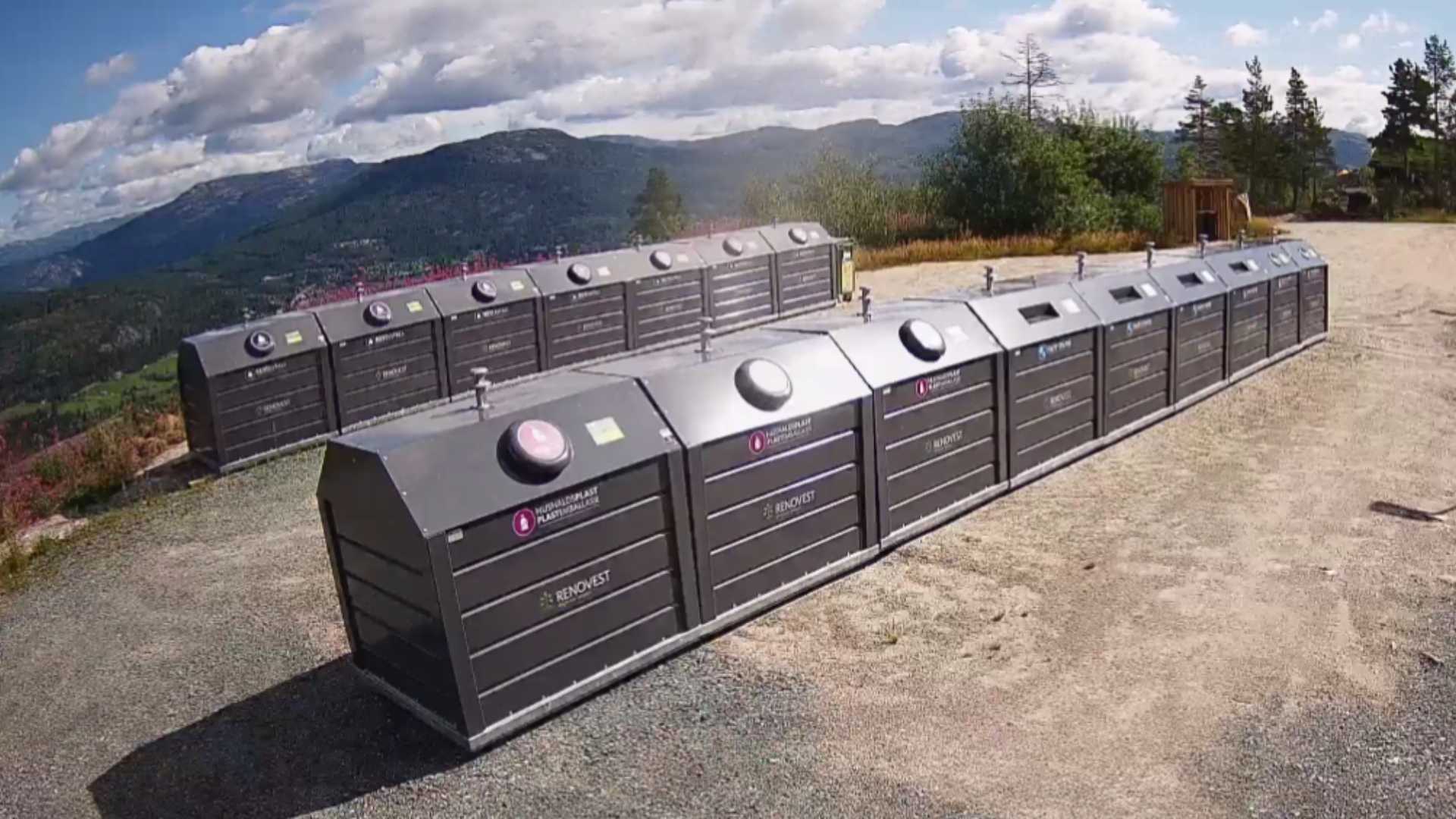Resirkuleringscontainere på fjellet under en blå himmel med fjellandskap i bakgrunnen.