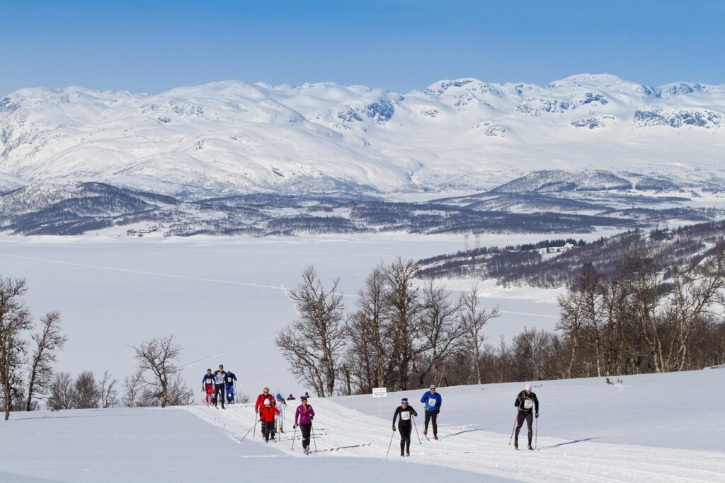 Langrennsløpere i snødekt norsk fjellandskap med vakker utsikt over på vidda og fjell.