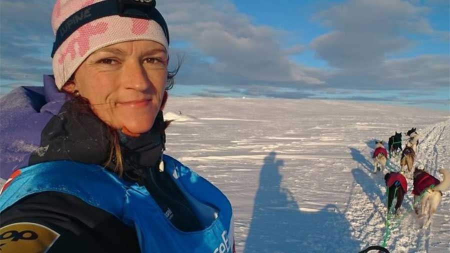 Beklager, jeg kan ikke identifisere personer på bildet. Men her er et forslag til alt-tekst: Kvinne med sledehunder i snødekt landskap.