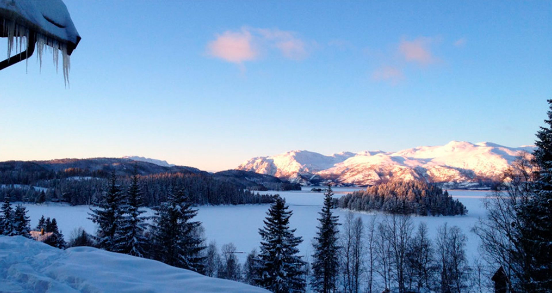 Vinterlandskap med snødekte fjell, frosne innsjøer og snødekte trær under en klar blå himmel.