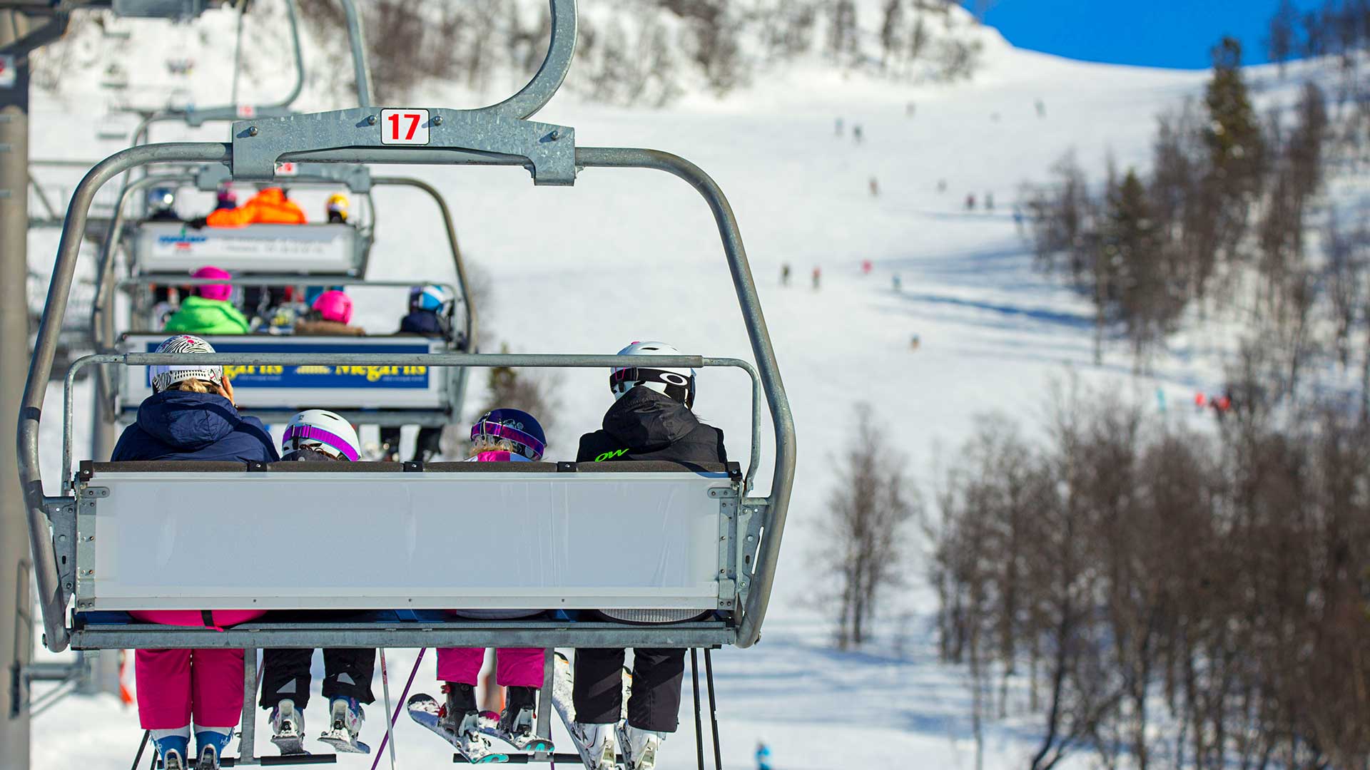 Tre syklister på en grusvei ved en innsjø, omgitt av grønt landskap og fjell i bakgrunnen.
