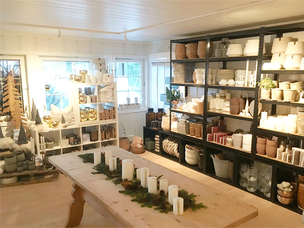Koselig interiørbutikk med lys og dekorasjoner på trebord, hyller fulle av, krukker og lys i naturlige farger.