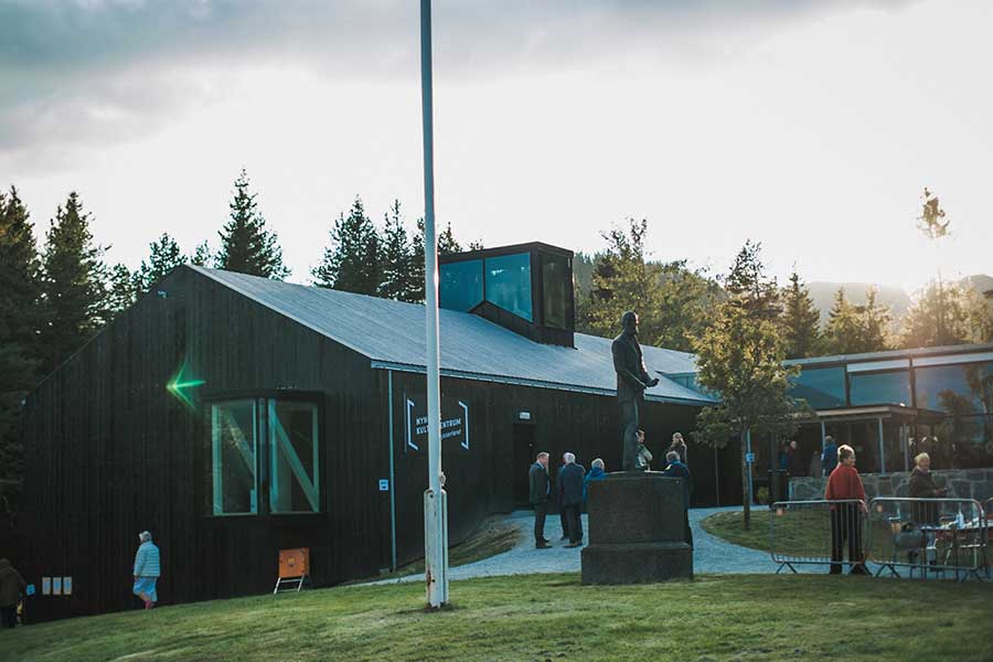 Kulturhus i skoglandskap ved solnedgang med mennesker utenfor.