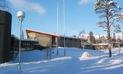 Moderne bygning i snødekt landskap med furutrær om vinteren under en klar blå himmel.