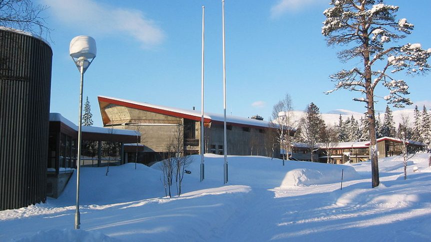 Moderne bygning i snødekt landskap med furutrær om vinteren under en klar blå himmel.