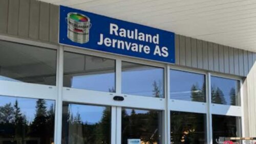 Inngangsdør til Rauland Jernvare AS-butikken med blått skilt og fjellrefleksjoner i glass.