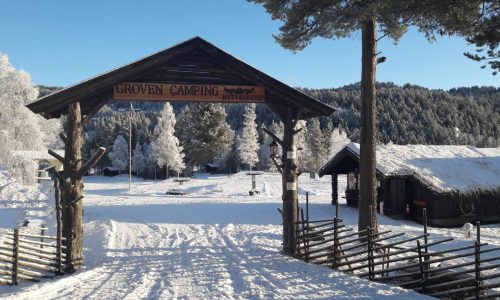 Snødekt inngang til Groven Camping Hyttegrend med vinterlandskap og frostdekte trær i bakgrunnen.