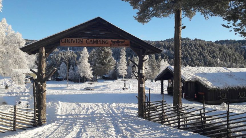Snødekt inngang til Groven Camping Hyttegrend med vinterlandskap og frostdekte trær i bakgrunnen.