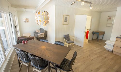 Lyst og moderne spisestue med stort tregulv, spisebord og designerlampe.