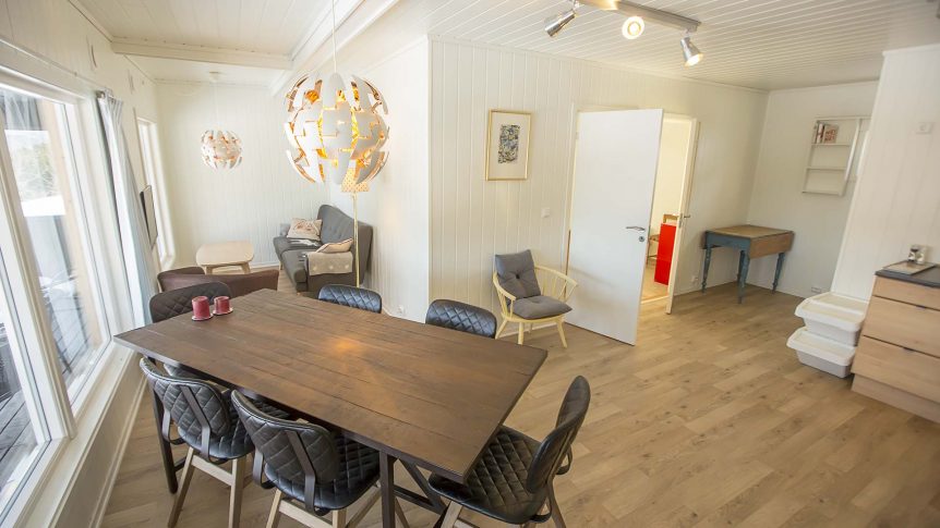 Lyst og moderne spisestue med stort tregulv, spisebord og designerlampe.