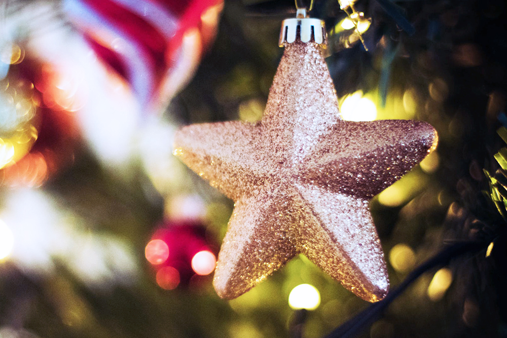 Gullstjerne julepynt på juletre, glitrende med vinterlys i bakgrunnen.