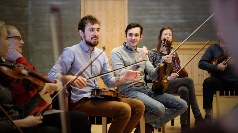 Gruppe musikere spiller fiolin sammen i en øvingssal, deltar i en workshop eller musikkøvelse.