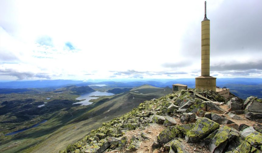 Utsikt fra Gaustatoppen med telekommunikasjonstårn og fjellandskap i bakgrunnen, klart vær og imponerende natur.