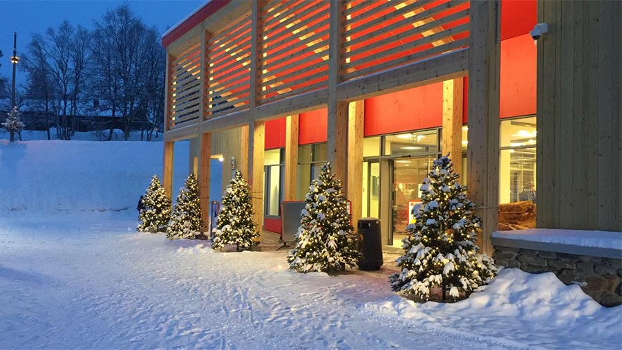 En moderne bygning pyntet til jul med snødekte juletre utenfor i vinterlandskap.