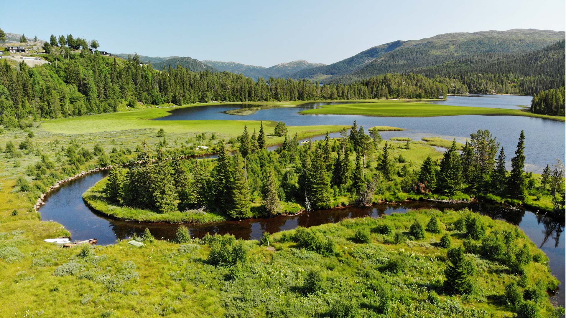 Grønn skogkledd innsjø med slyngende elv og fjell i bakgrunnen, norsk natur om sommeren.