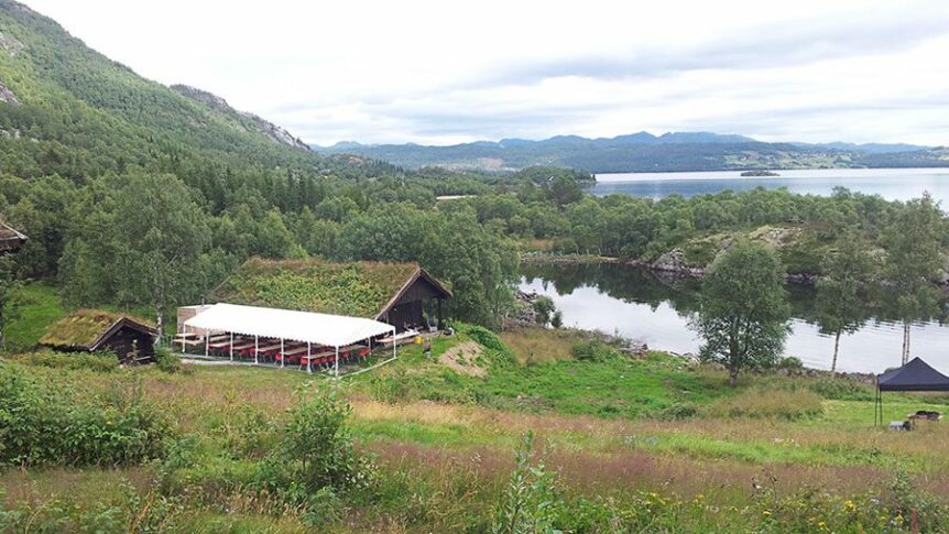 Gressdekkede hytter ved en innsjø omgitt av skog og fjell i Norge. Naturskjønn utsikt og fredelig landskap.