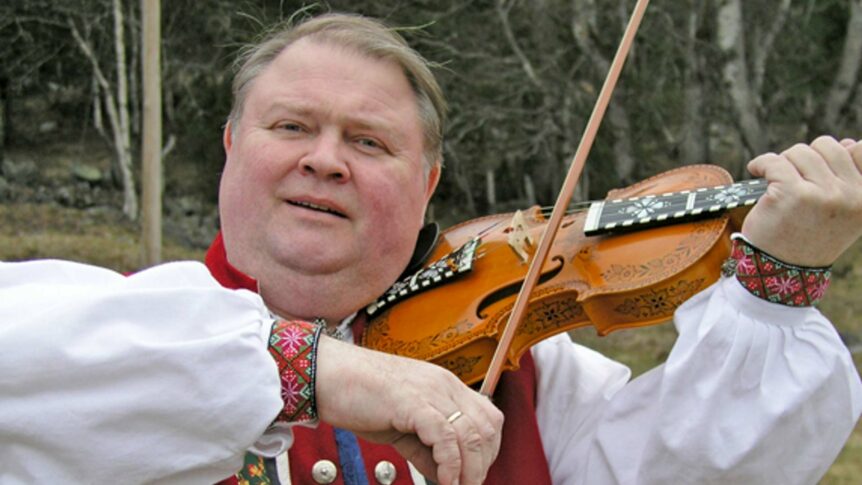 Mann spiller hardingfele i tradisjonell bunad utendørs, norsk folkemusikk.