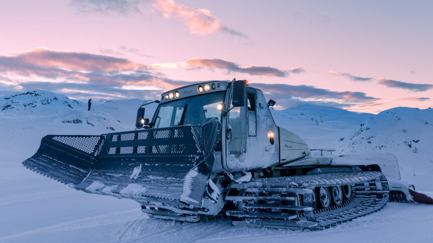 Snøplog på fjellandskap i solnedgang, klar for å rydde snødekte veier i vinternaturen.