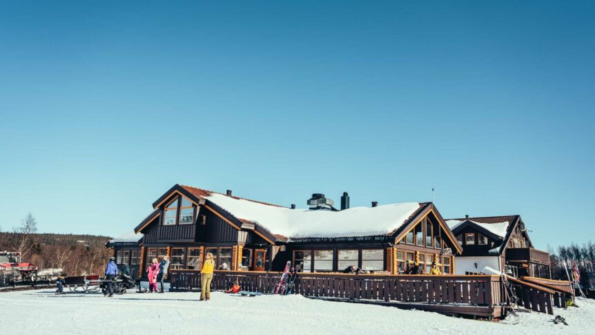 Skihytte på snødekt fjell, folk i varme klær. Klart blått himmel. Vinterdag i Norge.