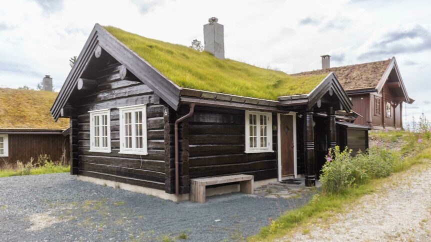Tradisjonell norsk tømmerhytte med torvtak i naturskjønne omgivelser på en overskyet dag.