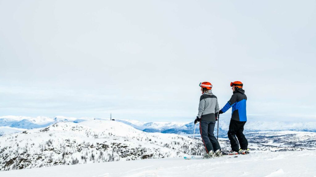 To skiløpere på fjellet ser utover snødekte landskap i Norge.