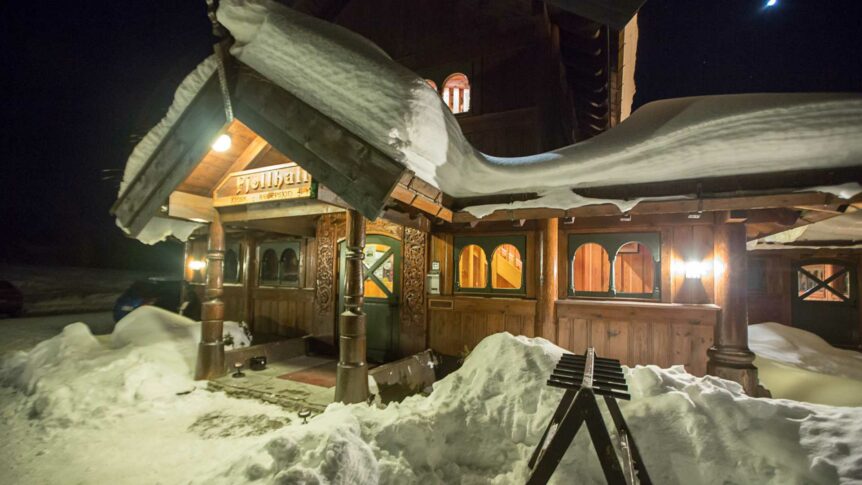 Koselig fjellhytte dekket av snø om kvelden, med lysende lamper og tradisjonell norsk arkitektur.