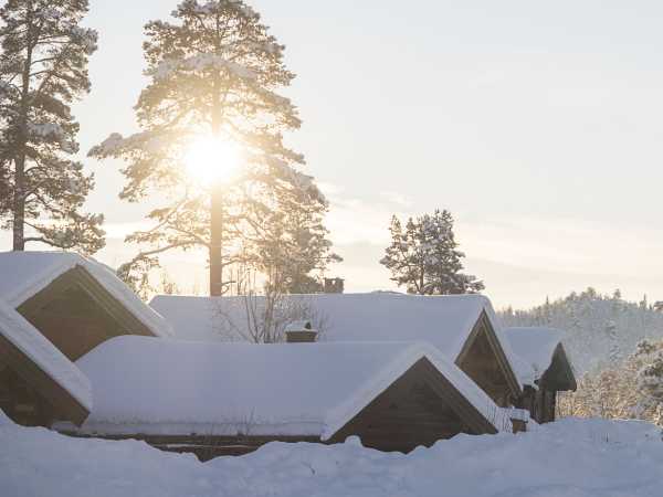 Snødekte hytter i vintersol, omgitt av trær i et nordisk landskap.