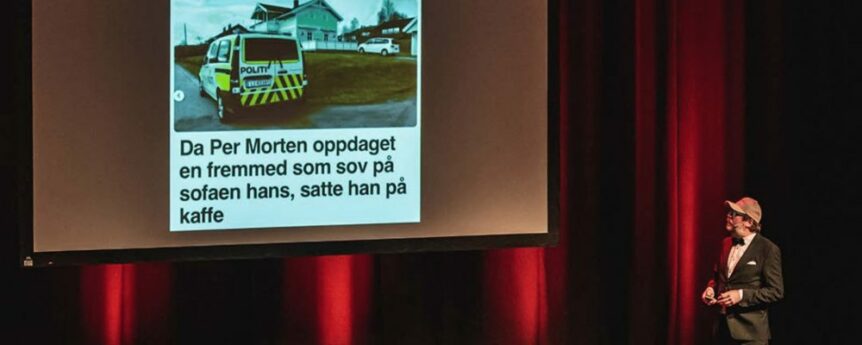 En presentatør står på scenen med en lysbildefremvisning, som viser en avisartikkel med bilde av en politibil.