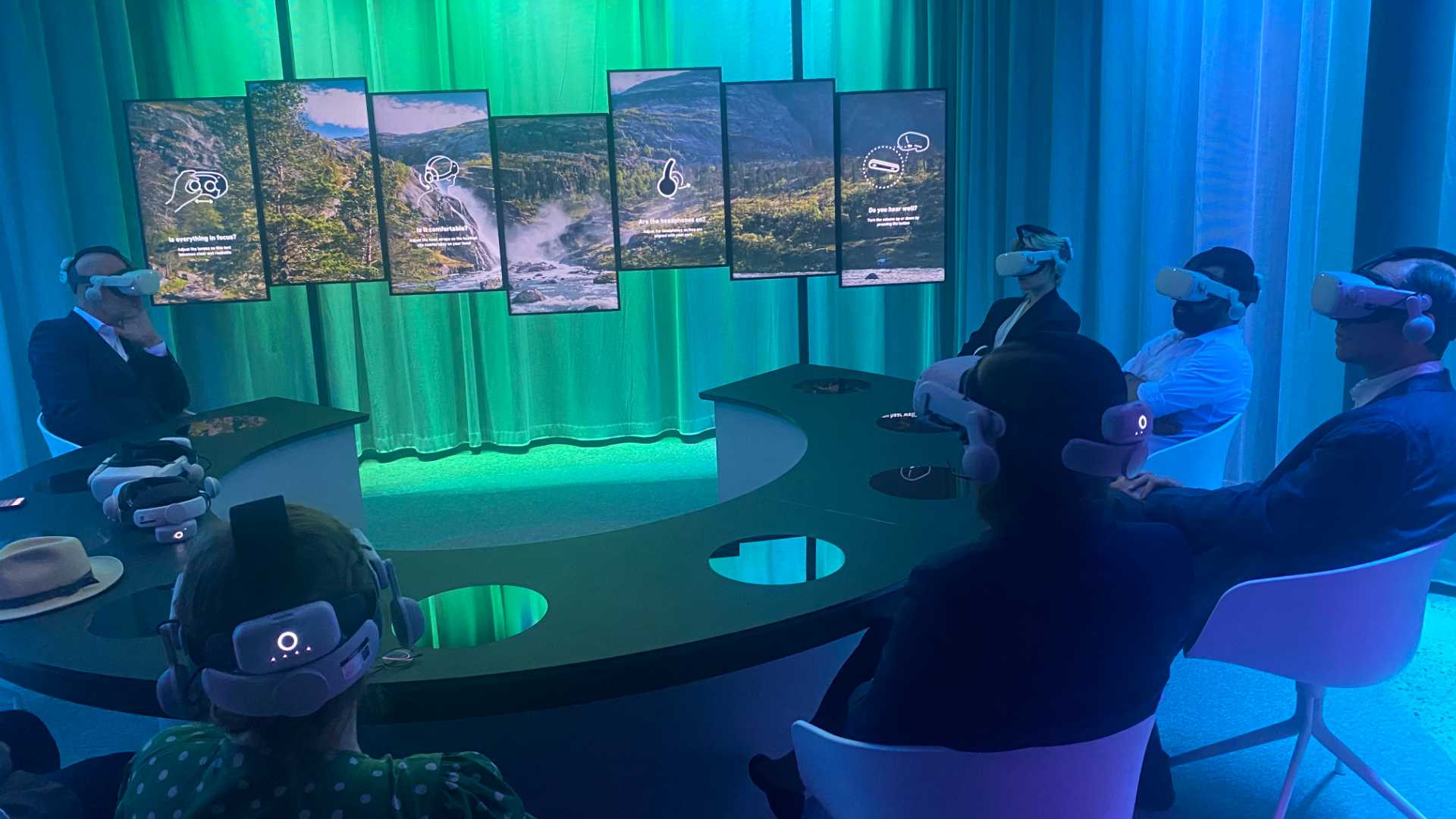 Personer som bruker VR-briller i futuristisk møte, omgitt av skjermer med naturbilder i forskjellige farger.