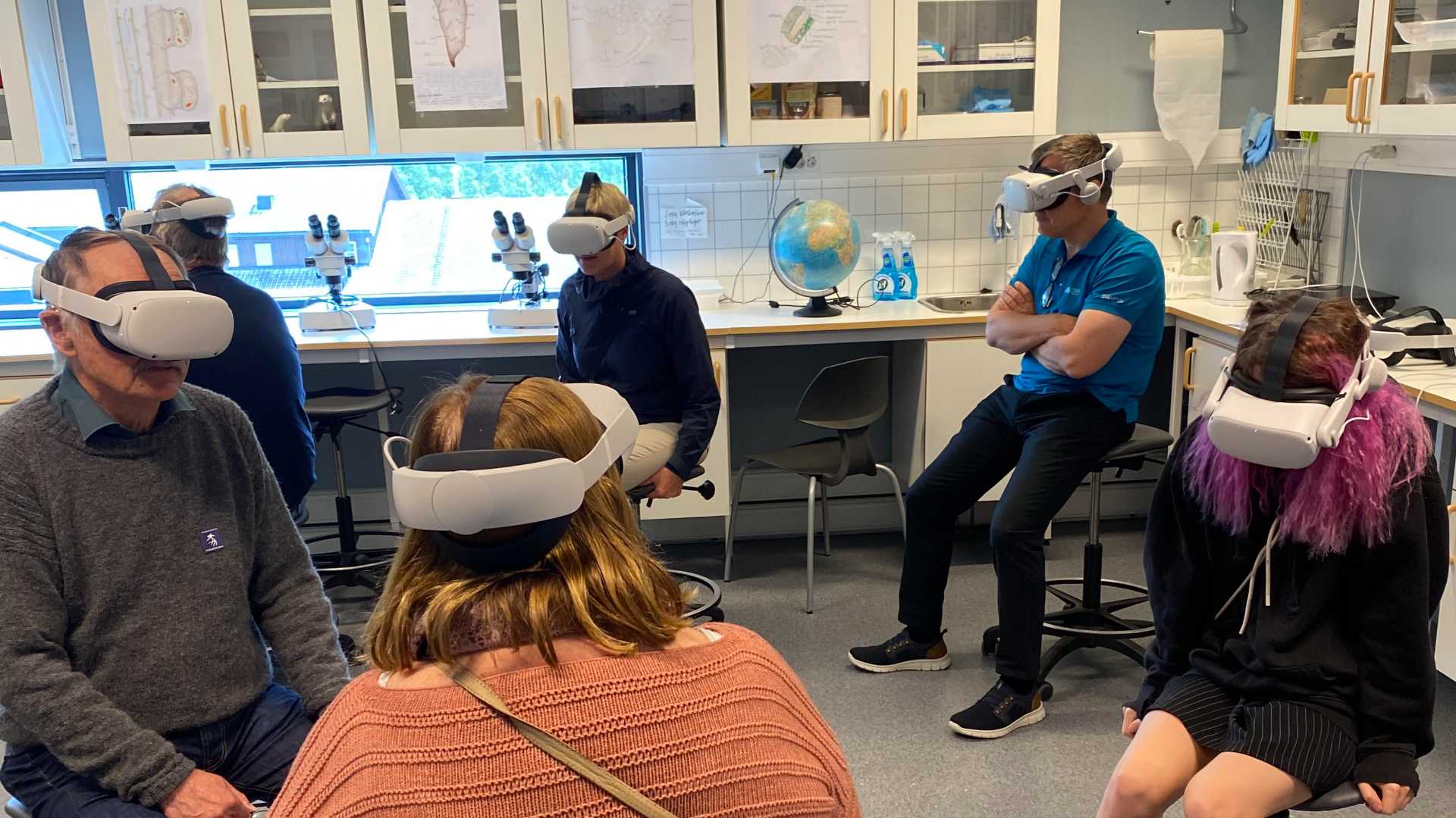 Mennesker med VR-briller utforsker virtuell virkelighet i et laboratorium med mikroskop og kart.