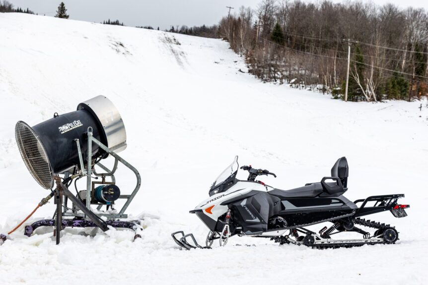 Snøscooter parkert ved siden av snøkanon i vinterlandskap.